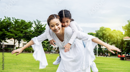 Cute asian mother and little daughter have fun in park together at sunset. They run, fly like a plane, kiss and have fun together. Happy family
