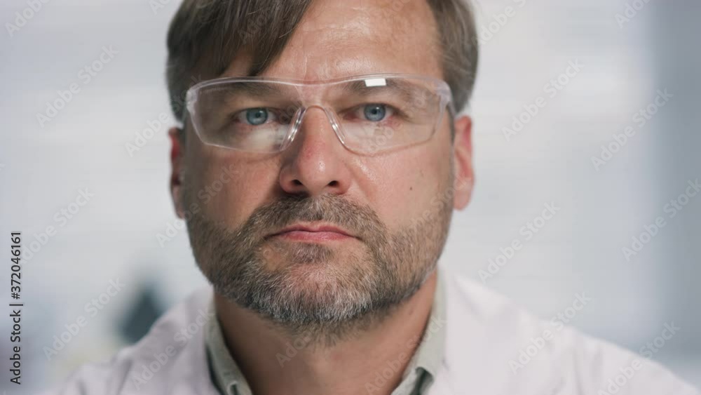 Portrait shot of bearded male biomedical scientist in gloves and goggles taking off face mask and looking at camera Portrait shot of bearded male biomedical scientist in gloves and goggles taking off face mask and looking at camera