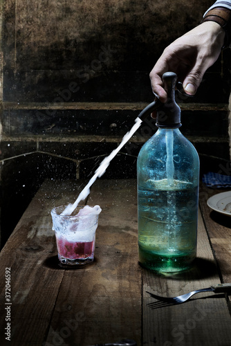 Photos A male hand using a siphon bottle to mix soda into glass of wine in a tavern of antique ambiance