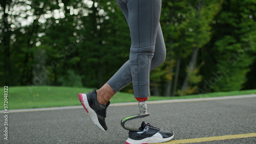 Female runner with artificial limb exercising in park.Girl legs running outdoors