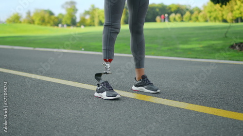 Jogger with artificial limb standing in park. Woman at start position on road