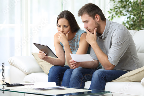 Fotografia Worried couple comparing receipt on tablet at home