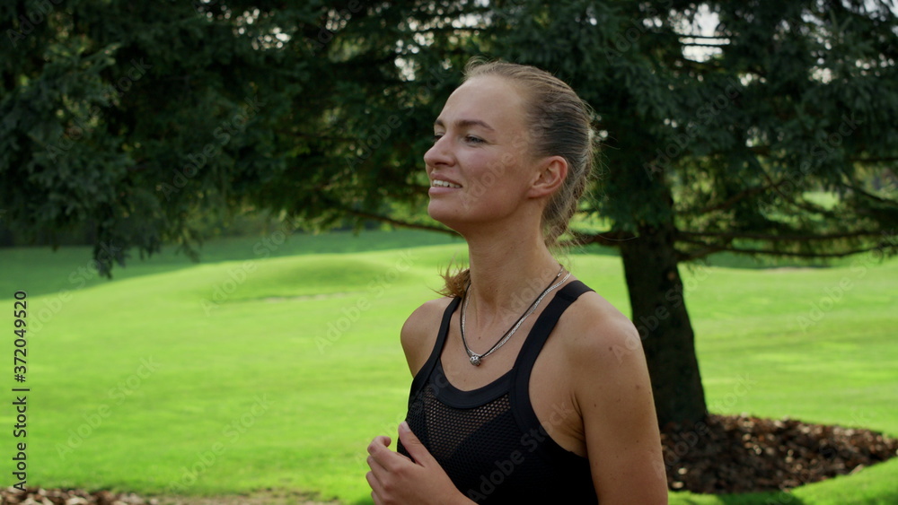 Positive woman running in green park. Athlete doing cardio workout at morning Positive woman running in green park. Athlete doing cardio workout at morning