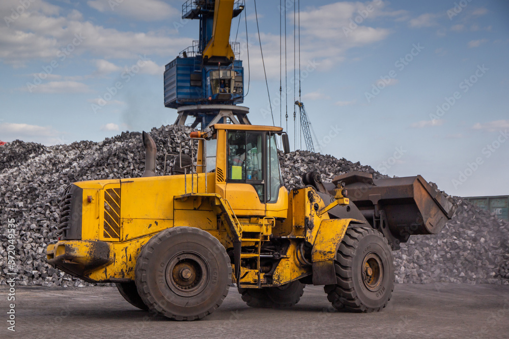 A bucket loader carries out loading of coal in an open port warehouse on a background of black mountains of coal