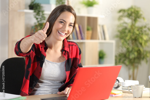 Happy student girl with laptop doing thumbs up at home photo