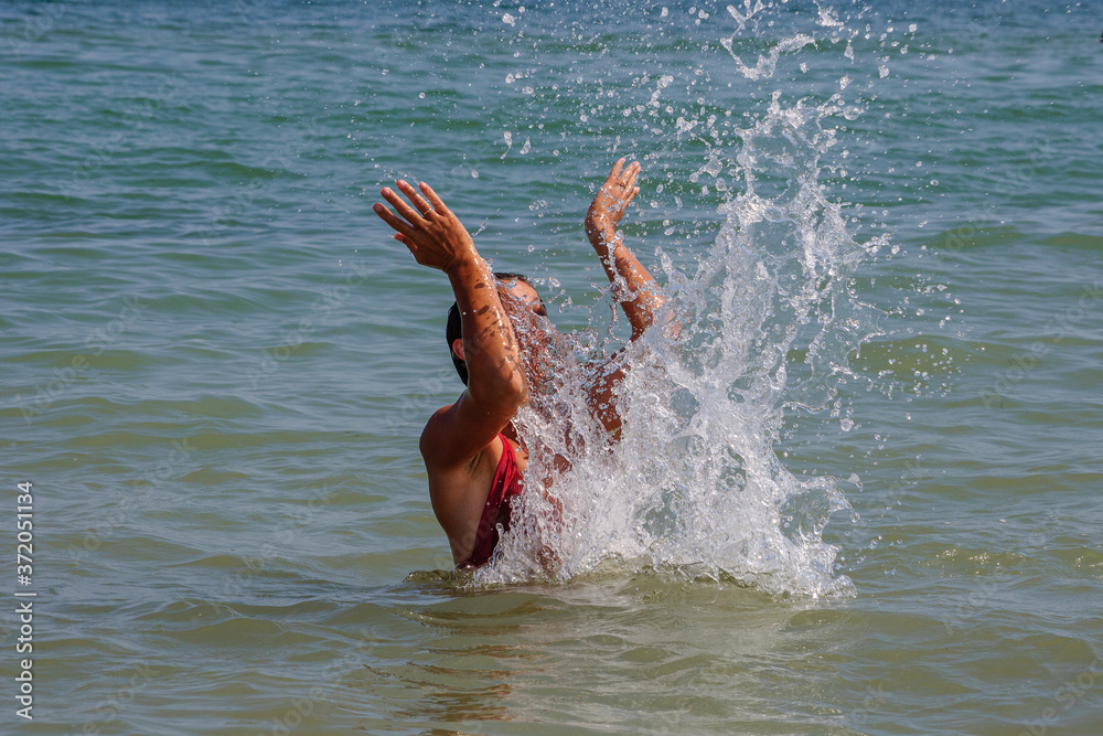 Young girl makes splashes with her hands and bathes in the waves