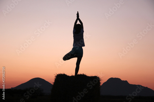 Young girl practices yoga at sunset against the background of mountains.