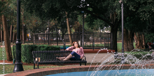 Woman sitting on a bench in Downtown winter park in park ave in Orlando florida in the fall wearing a sweater and boots by a fountain  photo