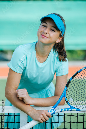Portrait of a teenage girl standing tennis court, leaning on the net, © zzzdim