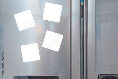 Four blank white magnet notes attached on gray refrigerator door photo