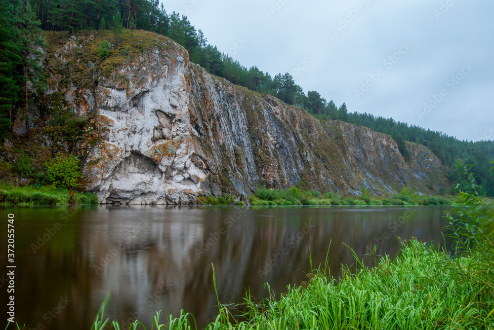 Beautiful river landscape with forest slopes of mountains. Limestone rocks in the Ural mountains. Cloudy sky in the background. Beautiful river landscape with forest slopes of mountains. Limestone rocks in the Ural mountains. Cloudy sky in the background.