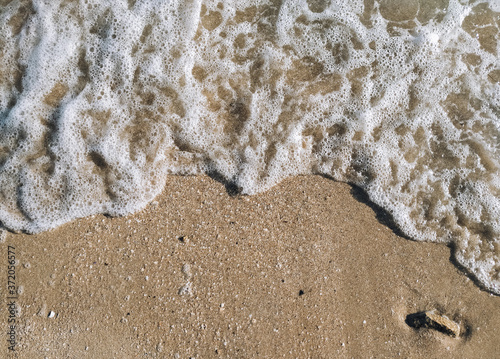 Beautiful sea wave on a yellow sandy beach with white clean foam. Copy space, top view.