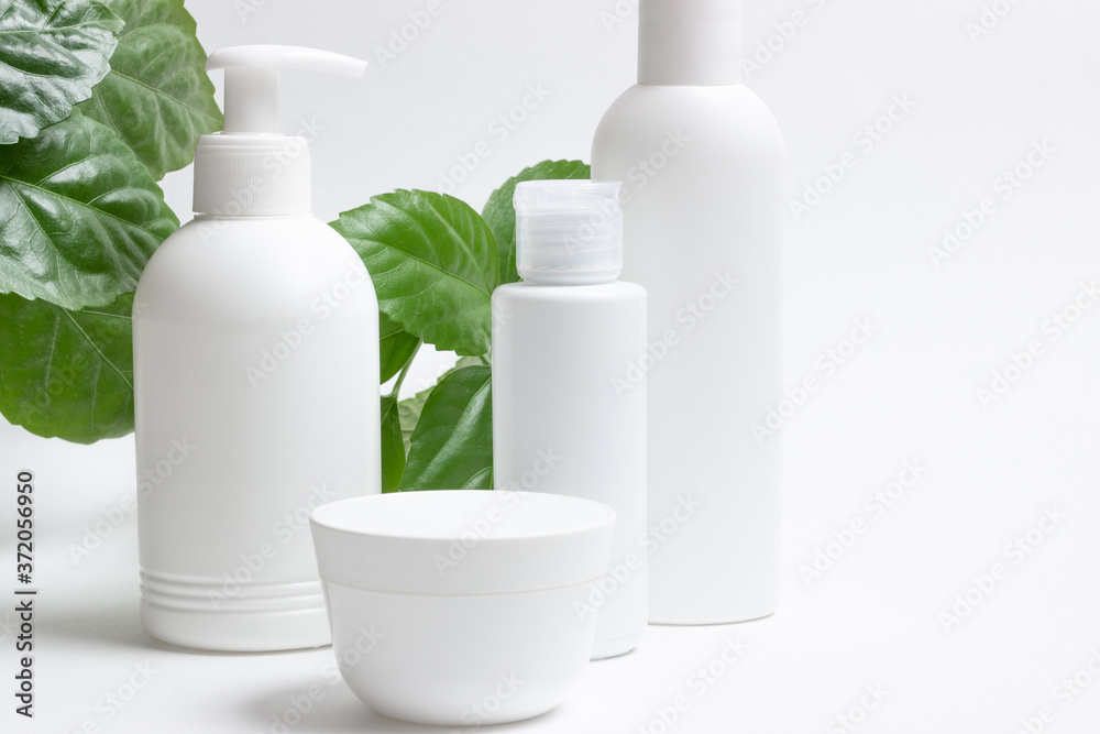 Set of cosmetic cans of organic cosmetics for face and body care on a white background with green leaves. Cream, shampoo and lotion on a light background. Layout, copy space. Set of cosmetic cans of organic cosmetics for face and body care on a white background with green leaves. Cream, shampoo and lotion on a light background. Layout, copy space.