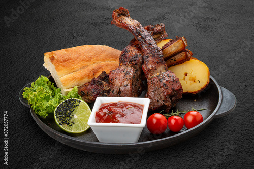 Grilled lamb rack with baked potatoes, matnakash and red sauce. Served in a cast iron pan photo