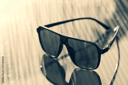 Retro aviator sunglasses model with black lenses and black frame plastic material reflecting the sun in a summer day closeup . Selective focus