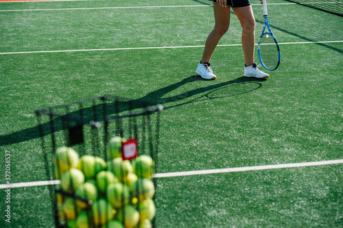 Tennis ball basket and feet of a girl training next to it. photo