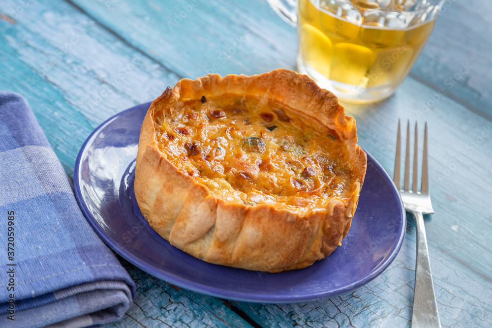 A quiche on a blue rustic table with a jar of beer A quiche on a blue rustic table with a jar of beer