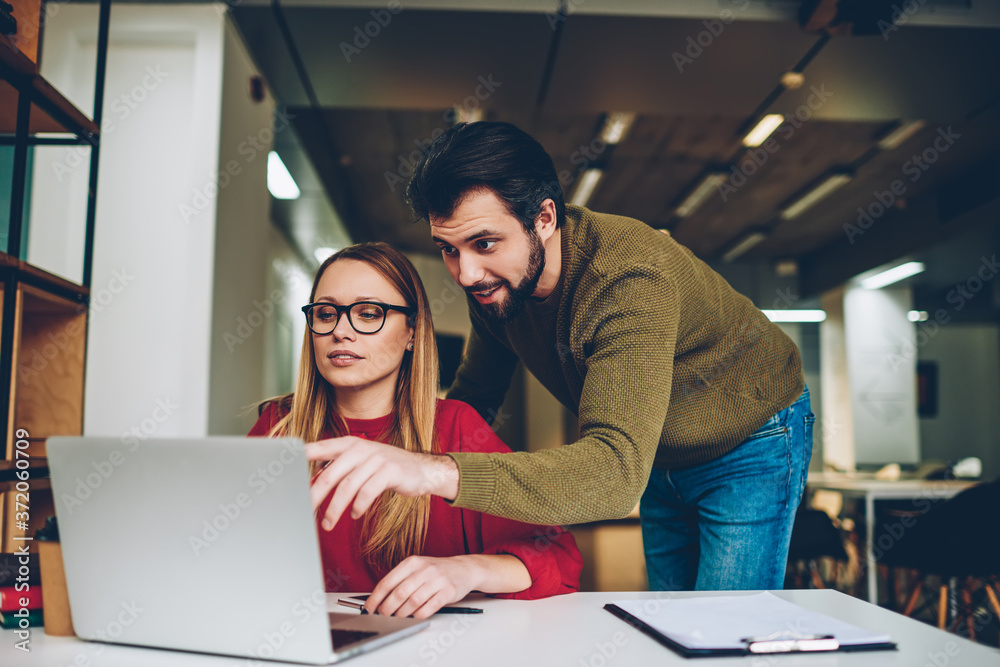 Shot of business man and woman looking at computer monitor and reading news, focused team working together in office while feeling shock of receiving message from friend at laptop application indoors Shot of business man and woman looking at computer monitor and reading news, focused team working together in office while feeling shock of receiving message from friend at laptop application indoors