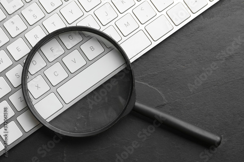 Magnifier glass and keyboard on black slate background, flat lay. Find keywords concept photo