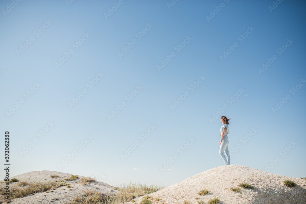 a young, beautiful girl stands on the top of a white mountain against the background of the sunset
