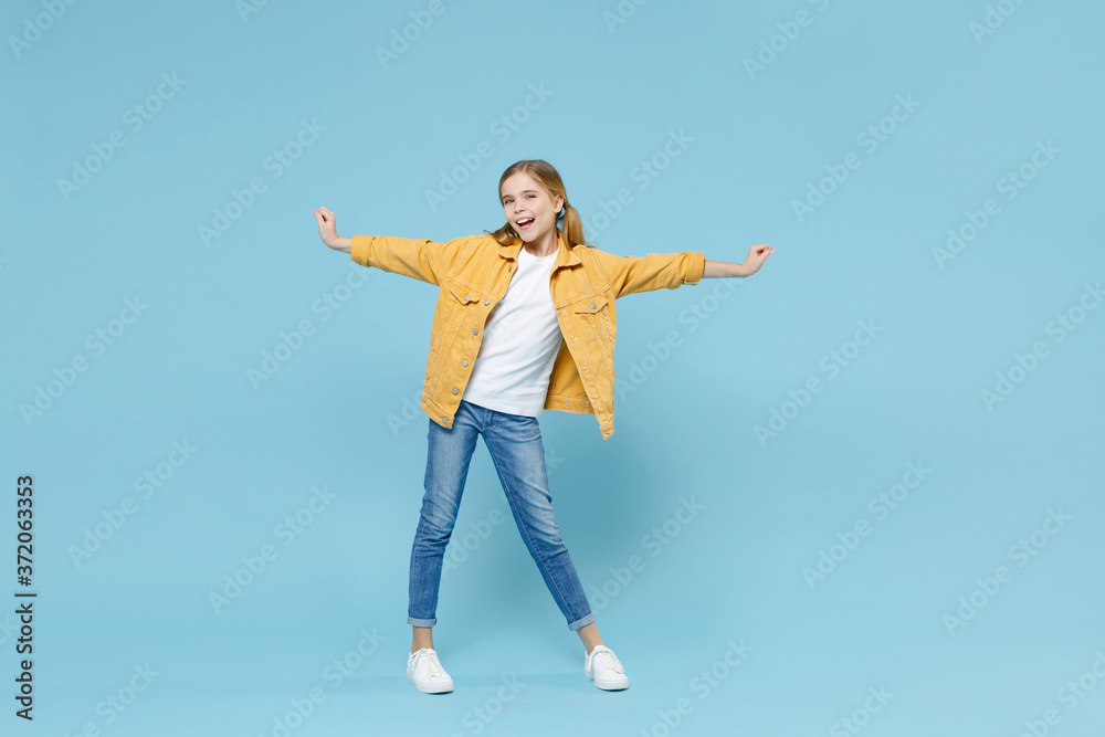 Full length portrait of cheerful little blonde kid girl 12-13 years old in yellow jacket isolated on blue background studio portrait. Childhood lifestyle concept. Mock up copy space. Spreading hands. Full length portrait of cheerful little blonde kid girl 12-13 years old in yellow jacket isolated on blue background studio portrait. Childhood lifestyle concept. Mock up copy space. Spreading hands.