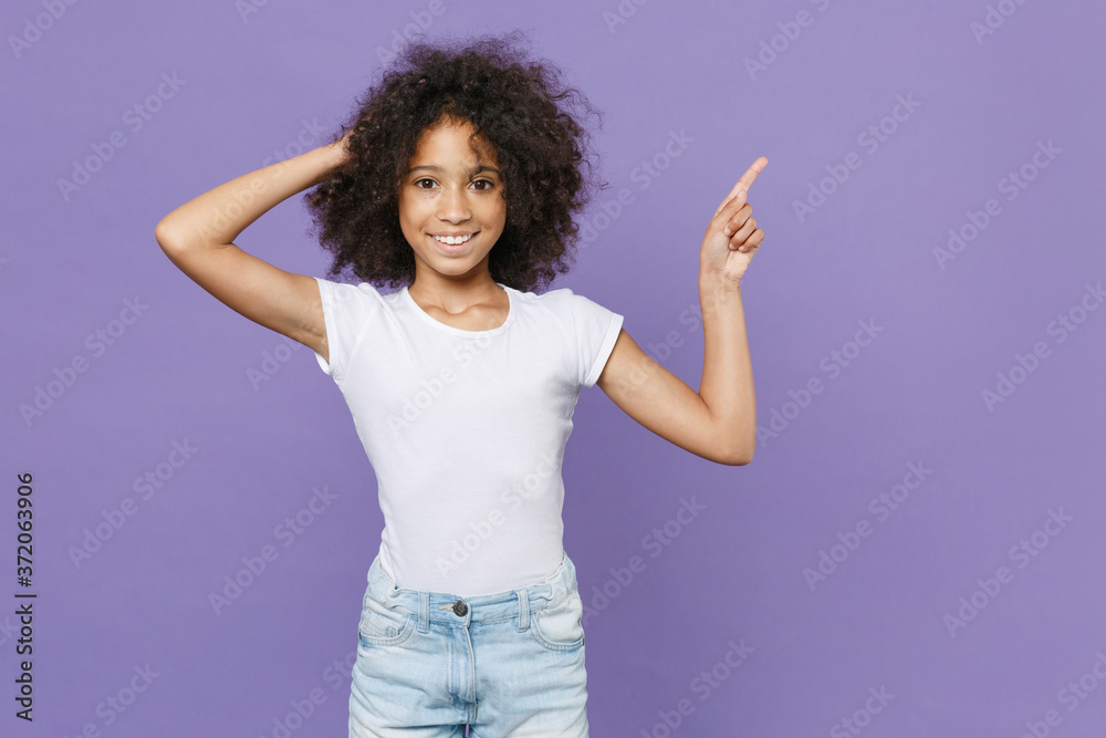 Smiling little african american kid girl 12-13 years old in white t-shirt isolated on violet wall background studio portrait. Childhood lifestyle concept. Pointing index finger up, put hand on head. Smiling little african american kid girl 12-13 years old in white t-shirt isolated on violet wall background studio portrait. Childhood lifestyle concept. Pointing index finger up, put hand on head.
