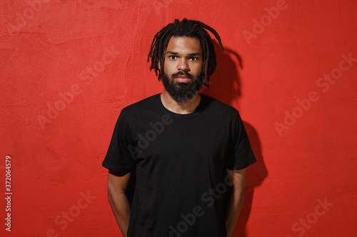 Canvas-taulu Handsome attractive young african american man guy with dreadlocks 20s wearing black casual t-shirt posing looking camera isolated on bright red color wall background studio portrait