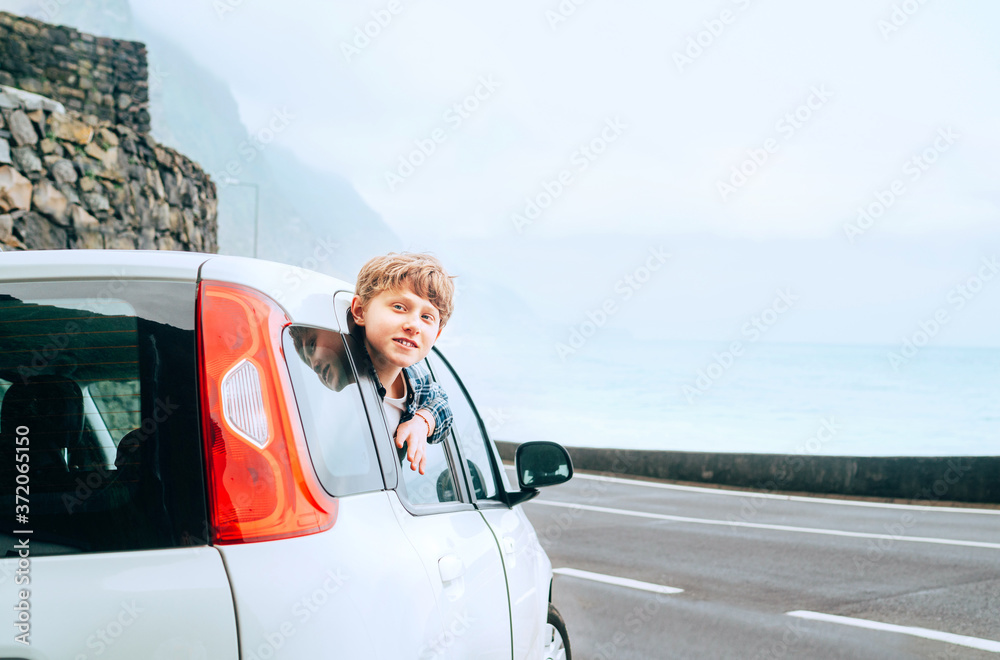 Blonde hair teenager boy looking out from the rear passangers door of economy class auto and smiling.Rental car and Traveling by auto concept image.