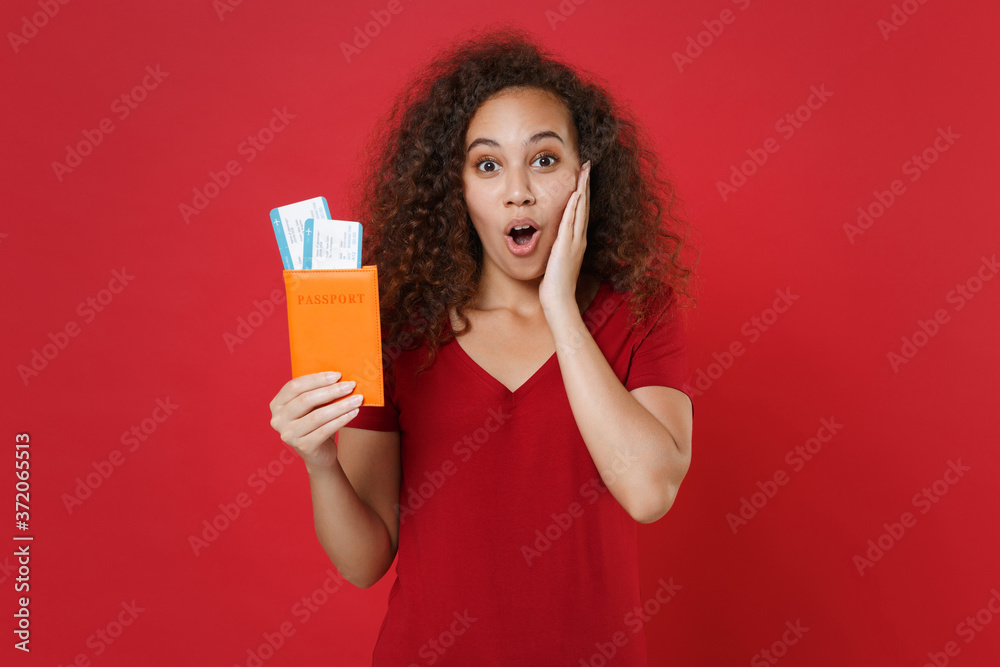 Shocked african american girl in casual t-shirt isolated on red background. Passenger traveling abroad travel on weekends getaway. Air flight journey concept. Hold passport tickets, put hand on cheek. Shocked african american girl in casual t-shirt isolated on red background. Passenger traveling abroad travel on weekends getaway. Air flight journey concept. Hold passport tickets, put hand on cheek.