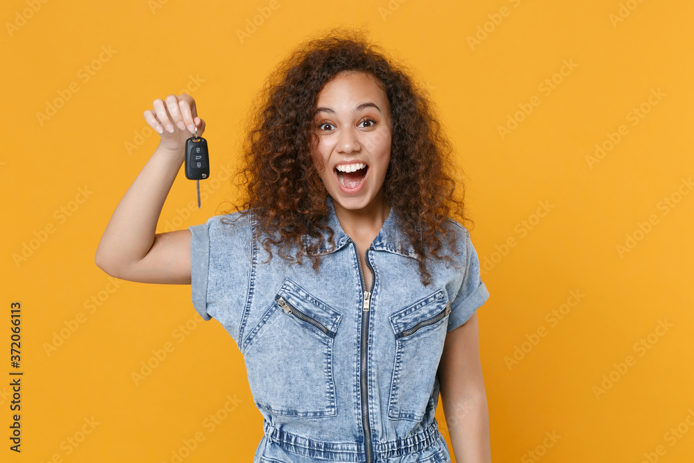 Surprised young african american girl in casual denim clothes posing isolated on yellow wall background studio portrait. People sincere emotions lifestyle concept. Mock up copy space. Hold car keys. - obrazy, fototapety, plakaty 