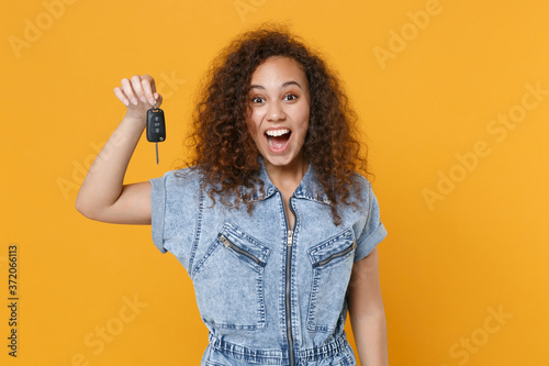 Surprised young african american girl in casual denim clothes posing isolated on yellow wall background studio portrait. People sincere emotions lifestyle concept. Mock up copy space. Hold car keys. photo