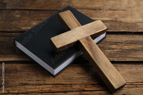 Christian cross and Bible on wooden background, closeup. Religion concept