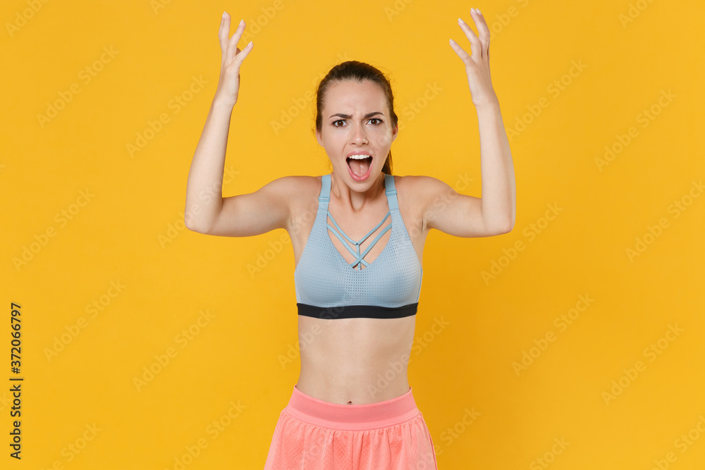 Angry young fitness sporty woman girl in sportswear working out isolated on yellow wall background. Workout sport motivation lifestyle concept. Mock up copy space. Screaming swearing spreading hands.