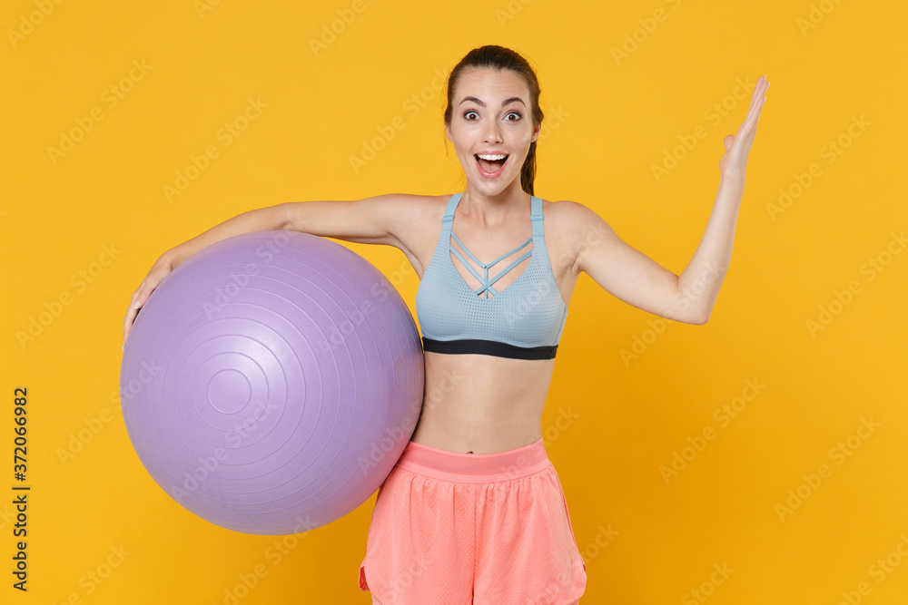 Surprised young fitness sporty woman in sportswear working out isolated on yellow wall background studio portrait. Workout sport motivation concept. Mock up copy space. Hold fitball, spreading hands. Surprised young fitness sporty woman in sportswear working out isolated on yellow wall background studio portrait. Workout sport motivation concept. Mock up copy space. Hold fitball, spreading hands.