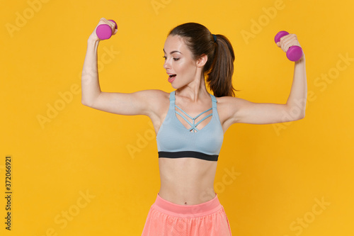 Shocked young fitness sporty woman girl in sportswear working out isolated on yellow background studio. Workout sport motivation lifestyle concept. Mock up copy space. Doing exercise with dumbbells.