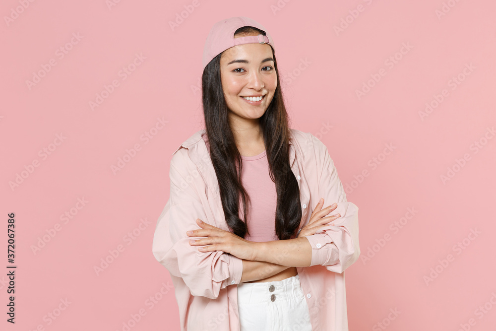 Smiling young asian woman girl in casual clothes cap posing isolated on pastel pink background studio portrait. People sincere emotions lifestyle concept. Mock up copy space. Holding hands crossed. Smiling young asian woman girl in casual clothes cap posing isolated on pastel pink background studio portrait. People sincere emotions lifestyle concept. Mock up copy space. Holding hands crossed.