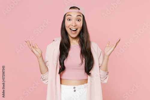 Surprised young asian woman girl in casual clothes cap posing isolated on pastel pink wall background studio portrait. People lifestyle concept. Mock up copy space. Keeping mouth open spreading hands.