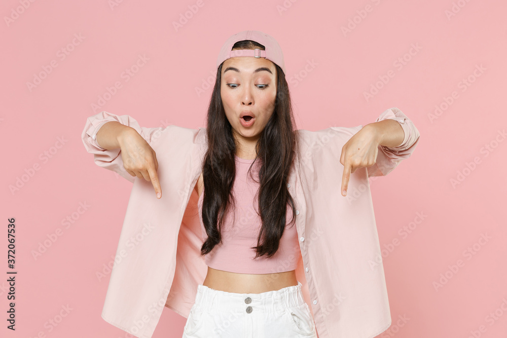 Shocked young asian woman girl in casual clothes cap posing isolated on pastel pink wall background studio portrait. People emotions lifestyle concept. Mock up copy space. Pointing index fingers down. Shocked young asian woman girl in casual clothes cap posing isolated on pastel pink wall background studio portrait. People emotions lifestyle concept. Mock up copy space. Pointing index fingers down.
