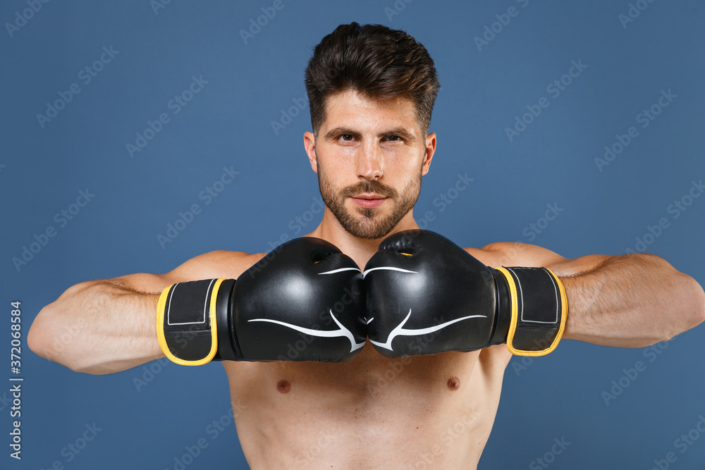 Confident young fitness sporty strong guy bare-chested muscular sportsman boxer isolated on blue background studio. Workout sport motivation lifestyle concept. Doing boxing exercises in boxing gloves. Confident young fitness sporty strong guy bare-chested muscular sportsman boxer isolated on blue background studio. Workout sport motivation lifestyle concept. Doing boxing exercises in boxing gloves.