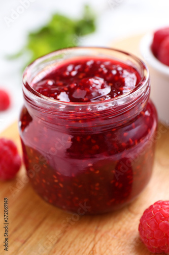 Delicious jam and fresh raspberries on wooden board, closeup