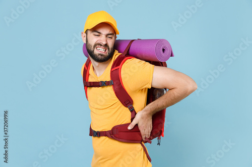 Sick traveler young man in yellow t-shirt cap backpack isolated on blue background. Tourist traveling on weekend getaway. Tourism discovering hiking concept. Feels bad pain spasm back sprain or neck.