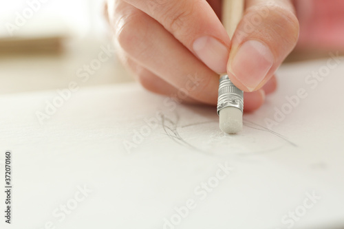 Woman correcting picture in notepad with pencil eraser, closeup