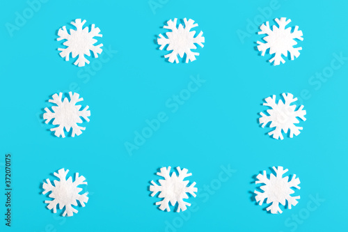 Frame of white snowflakes on a blue background. Snow and winter concept. New year and christmas concept. Beautiful winter background or card. Top view, flat lay, minimalism, copy space.