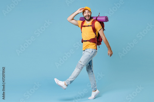 Full length portrait excited traveler man with backpack isolated on blue background. Tourist traveling on weekend. Tourism discovering hiking concept. Hold hand at forehead looking far away distance.
