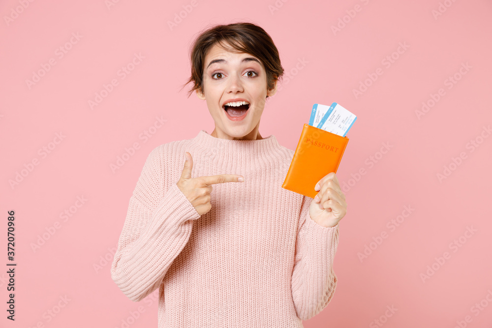 Excited young woman in casual sweater isolated on pastel pink background. Passenger traveling abroad to travel on weekends getaway. Air flight journey concept. Point index finger on passport tickets. Excited young woman in casual sweater isolated on pastel pink background. Passenger traveling abroad to travel on weekends getaway. Air flight journey concept. Point index finger on passport tickets.