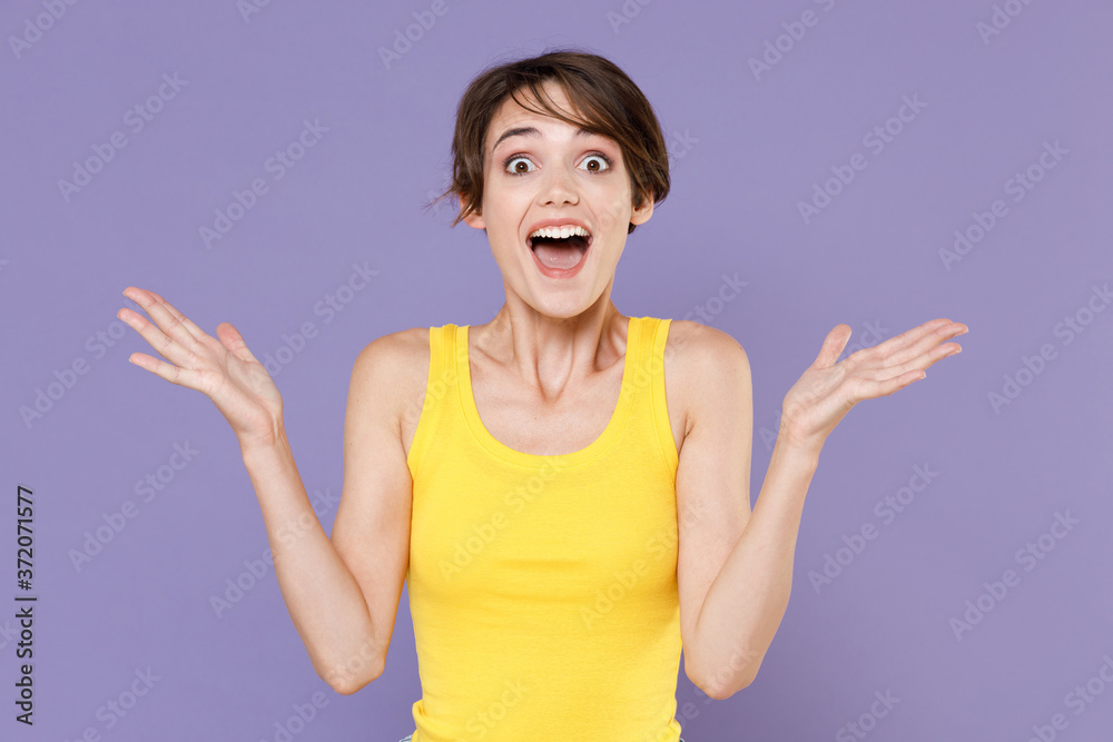 Surprised young brunette woman girl in yellow casual tank top posing isolated on pastel violet wall background studio portrait. People emotions lifestyle concept. Keeping mouth open, spreading hands. Surprised young brunette woman girl in yellow casual tank top posing isolated on pastel violet wall background studio portrait. People emotions lifestyle concept. Keeping mouth open, spreading hands.
