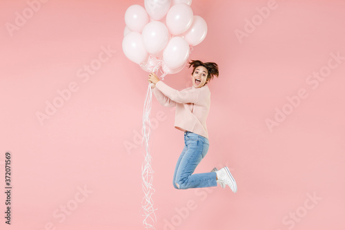 Full length portrait side view of surprised young woman in casual sweater isolated on pastel pink background. Birthday holiday party people emotions concept. Celebrating hold air balloons jumping.