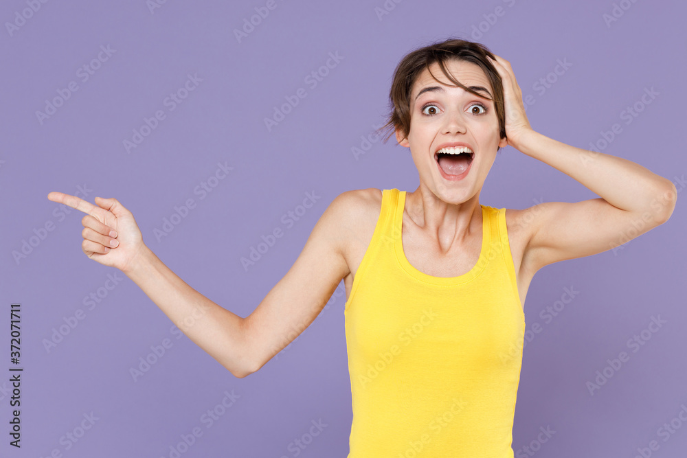 Surprised young brunette woman girl in yellow casual tank top posing isolated on pastel violet background. People lifestyle concept. Mock up copy space. Pointing index finger aside, put hand on head. Surprised young brunette woman girl in yellow casual tank top posing isolated on pastel violet background. People lifestyle concept. Mock up copy space. Pointing index finger aside, put hand on head.