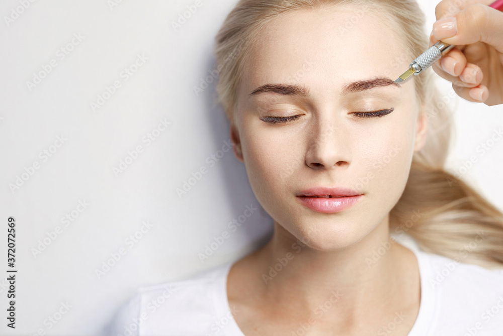Beautiful young girl with long eyelashes tweezing her eyebrows in a beauty salon. Woman doing eyebrow permanent makeup correction. Microblading brow.