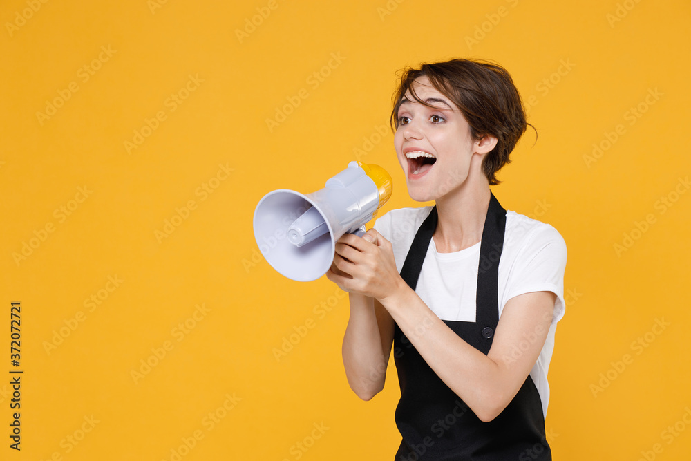 Excited cheerful young female woman 20s barista bartender barman employee wearing white t-shirt apron screaming in megaphone looking aside isolated on yellow color wall background studio portrait. Excited cheerful young female woman 20s barista bartender barman employee wearing white t-shirt apron screaming in megaphone looking aside isolated on yellow color wall background studio portrait.